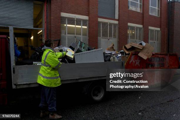 Scrap metal collectors searching through old office equipment in a skip, South London, UK.