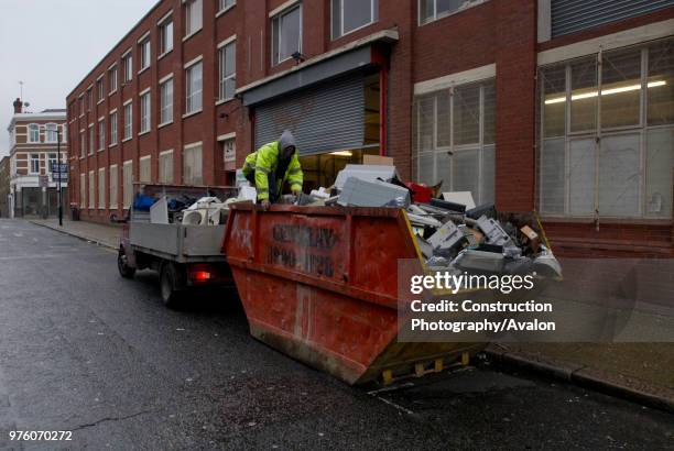 Scrap metal collectors searching through old office equipment in a skip, South London, UK.