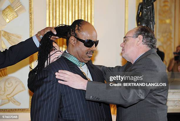 An official holds the hair of US music icon Stevie Wonder while French Culture minister Frederic Mitterrand awards him the Commandeur des Arts et des...