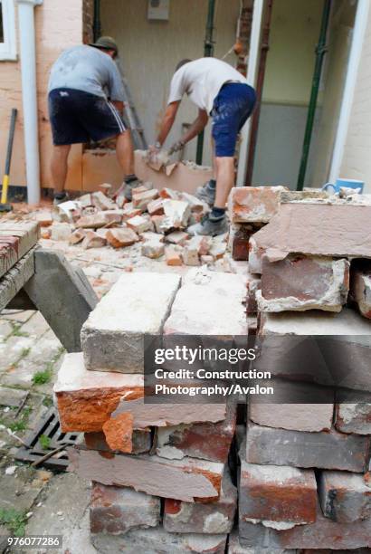 Men removing brick wall of house, UK.