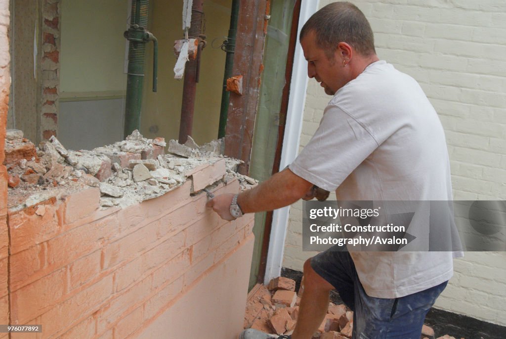 Man removing brick wall of house, UK