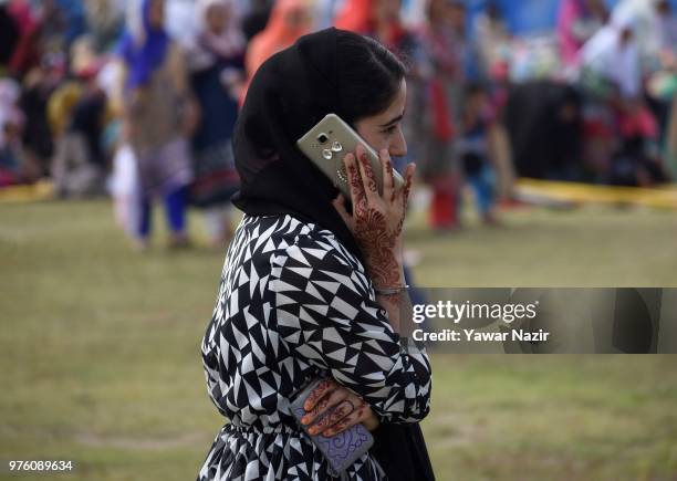 Kashmiri Muslim girl talks over phone as she waits for Eid-ul-Fitr prayers at Eid Gah on Eid-ul-Fitr, a festival of Muslims on June 16, 2018 in...