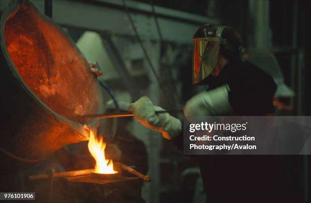 Steel worker in protective clothing working with furnace.