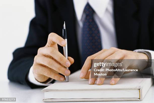 businessman's hands on book, holding pen, cropped view - studio legale foto e immagini stock