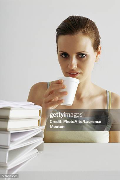 woman taking break, drinking from disposable cup, stack of binders in foreground - binders stockfoto's en -beelden