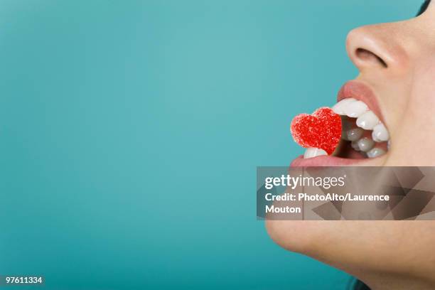 woman holding heart-shaped candy between teeth, cropped - gummy snoep stockfoto's en -beelden