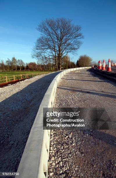 Half-battered road kerbs being laid on a verges of a new road.