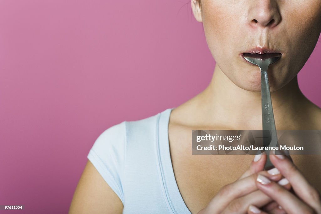 Woman licking spoon, cropped