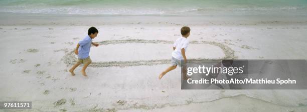 boys running on beach, chasing each other around circle drawn in sand - barefoot boy fotografías e imágenes de stock