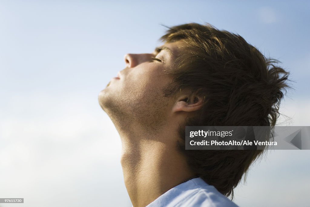 Young man outdoors with head back, eyes closed