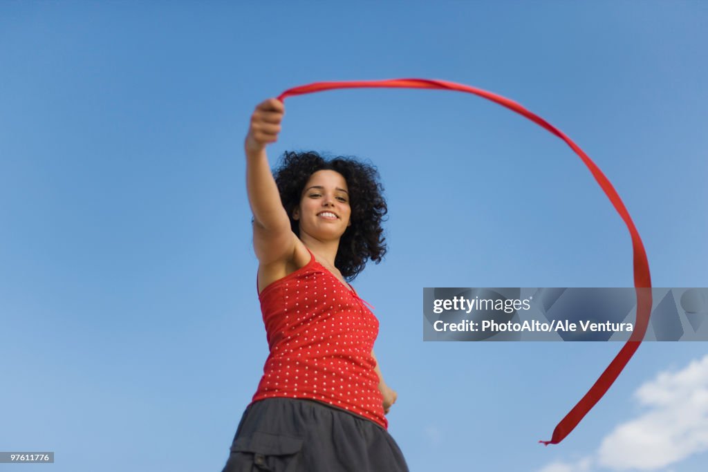 Young woman holding ribbon in wind, smiling, low angle view
