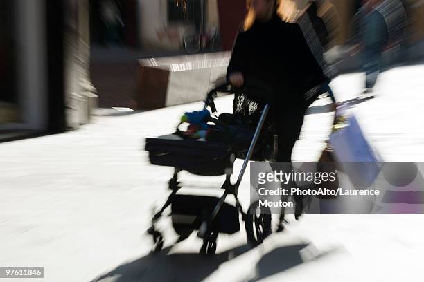 pedestrian pushing baby carriage on sidewalk, carrying shopping bags, blurred - mitziehen stock-fotos und bilder