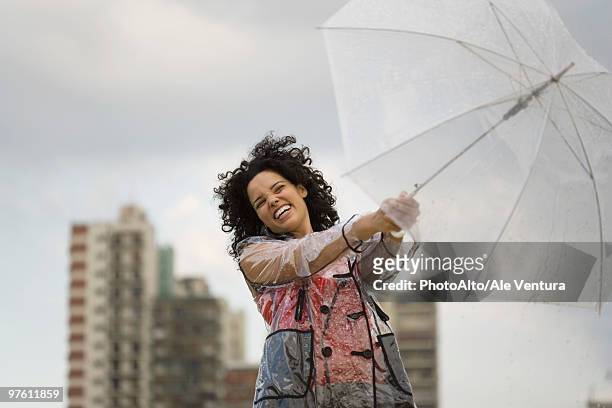 young woman holding onto umbrella on windy day, laughing - women wearing see through clothing stockfoto's en -beelden