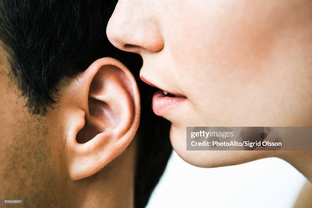 Woman whispering in man's ear, close-up