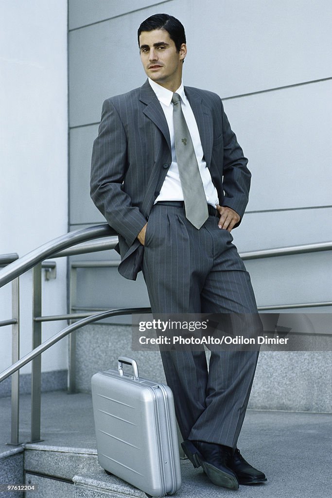 Businessman leaning against railing, briefcase on sidewalk at feet