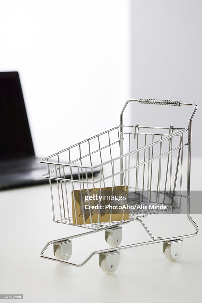 Credit card in miniature shopping cart, laptop computer in background