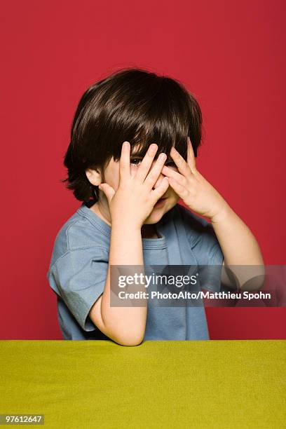 little boy covering face with hands, peeking through fingers at camera - guess who stock pictures, royalty-free photos & images