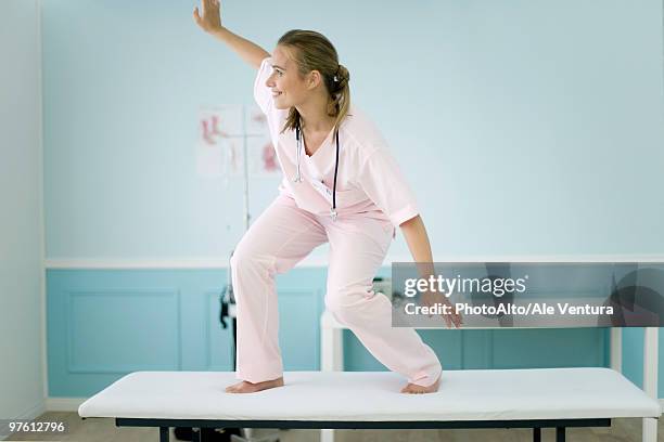 female medical student standing on top of examination table, pretending to surf - out of context fotografías e imágenes de stock