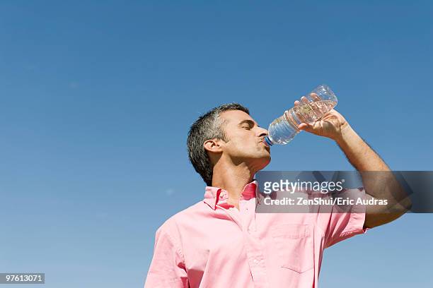 man standing outdoors drinking from bottle of water, low angle view, blue sky in background - man drinking water photos et images de collection