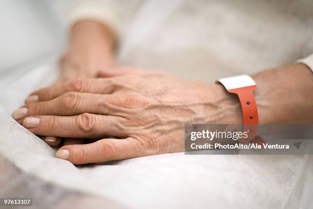 hospital patient's hands folded in lap, close-up - namensband stock-fotos und bilder