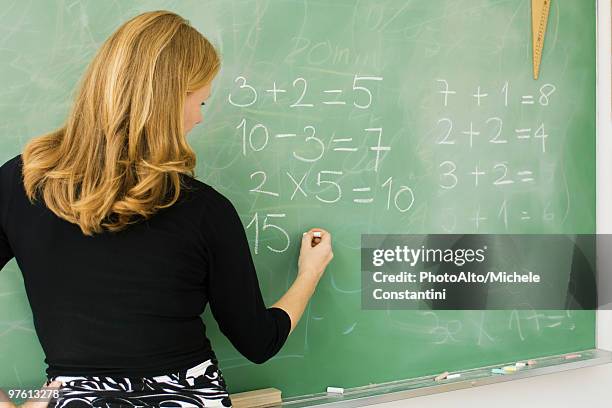 elementary teacher writing arithmetic on blackboard, rear view - educational subject stock pictures, royalty-free photos & images