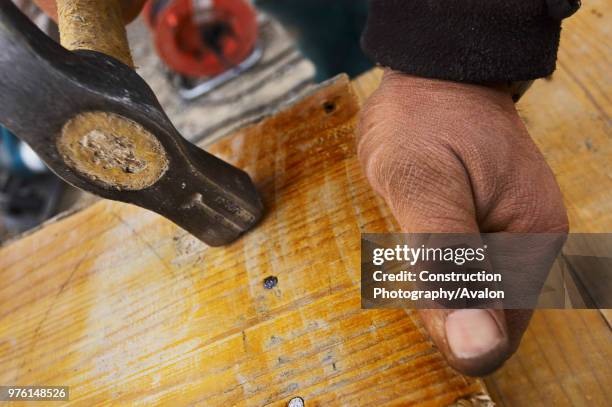 Carpenter hammering nails in to plank of wood.