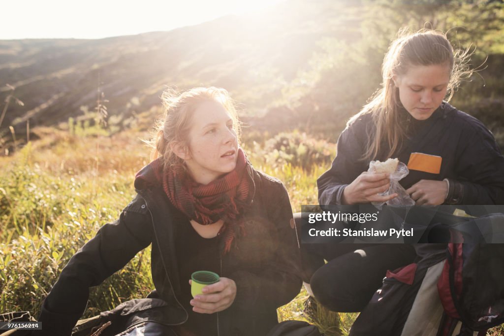 Two women taking break during trekking in mountains at sunset