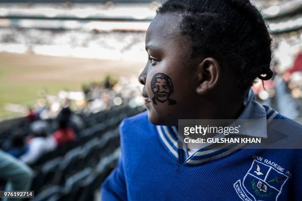 Young girl, with a temporary tattoo on her cheek showing the face of late South African anti-apartheid leader and statesman Nelson Mandela, attends...