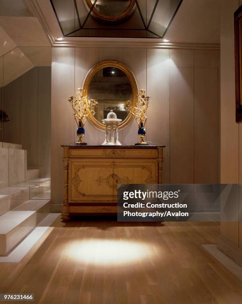 View of an ornate mirror and a wooden cabinet in an illuminated hallway.