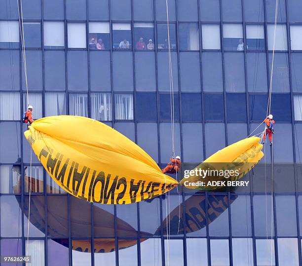 Employees look down through the windows as Indonesian Greenpeace activists hang a giant protest banner reading "plantations are not forests" on the...