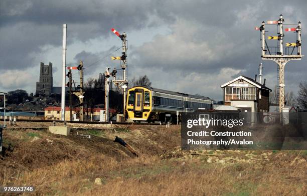 Semaphore signals at Ely Dock Junction as a Class 158 DMU passes with historic Ely cathedral in the background, circa 1993.