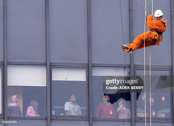 Employees watch as an Indonesian Greenpeace activist absiels in a furry orangutan suit to help hang a giant protest banner on the side of the...