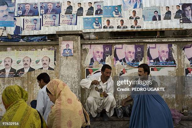 Afghan men drink tea as they sit next to a wall adorned with electoral posters in a street of Kabul on August 11, 2009. Afghans vote next week to...