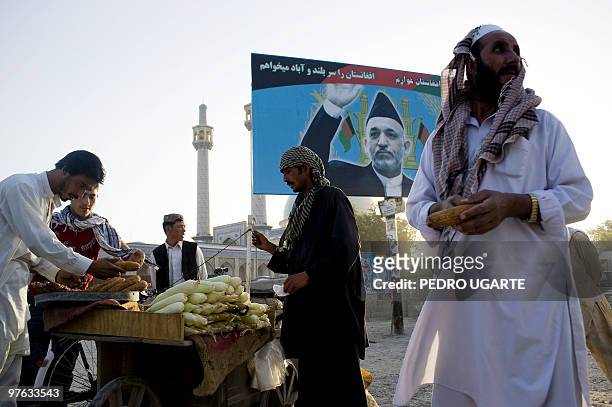 Afghans buy food on the street next to a billboard with a poster of incumbent President Hamid Karzai in Kabul on August 13, 2009. Afghans vote on...