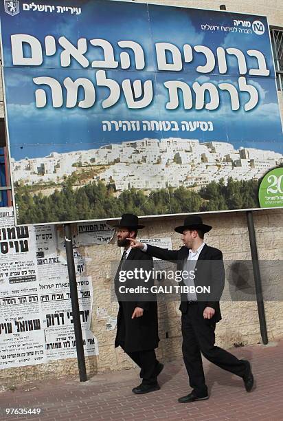 Israeli ultra-Orthodox Jewish men walk past a sign with the image of the east Jerusalem settlement of Ramat Shlomo, on March 11, 2010. Israeli Prime...