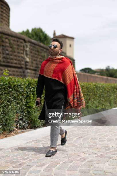 Guest is seen during the 94th Pitti Immagine Uomo wearing a red afghan with black tunic and grey pants on June 14, 2018 in Florence, Italy.