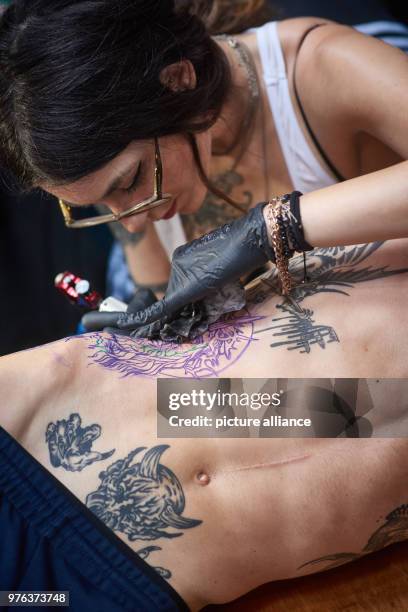 June 2018, Germany, Dortmund: Tattooist Sick Rose gives her customer Gaetan a tattoo in the form of Christ with a crown of thorns, at the...