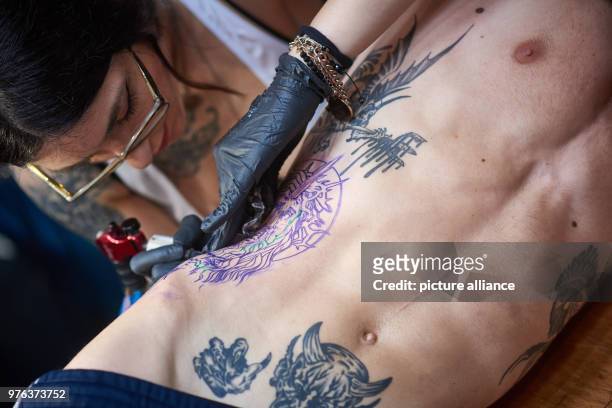 June 2018, Germany, Dortmund: Tattooist Sick Rose gives her customer Gaetan a tattoo in the form of Christ with a crown of thorns, at the...