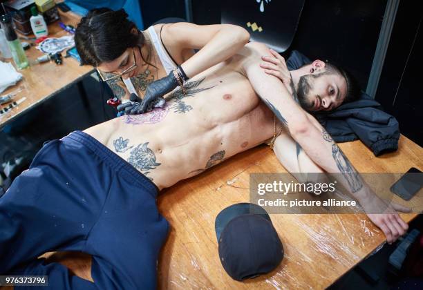 June 2018, Germany, Dortmund: Tattooist Sick Rose gives her customer Gaetan a tattoo in the form of Christ with a crown of thorns, at the...