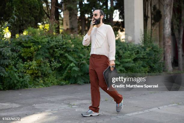 Guest is seen during the 94th Pitti Immagine Uomo wearing a cream shirt with chocolate pants and grey sneakers with black bag on June 14, 2018 in...