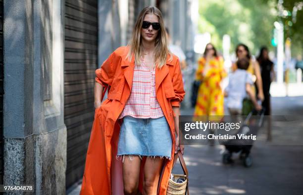 Guest wearing denim mini skirt, orange trench coat, Loewe bag is seen outside M1992 during Milan Men's Fashion Week Spring/Summer 2019 on June 16,...