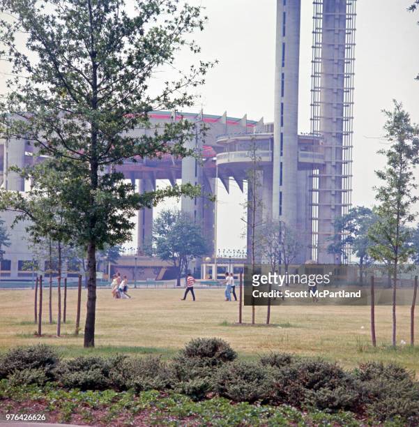 View of people on a lawn next to the World's Fair pavilion and observation towers, Flushing Meadows Corona Park, New York, New York, June 1, 1967.