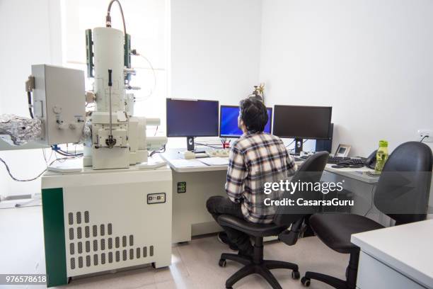 young male scientist using computer next to field emission electron microscope - computer scientist stock pictures, royalty-free photos & images