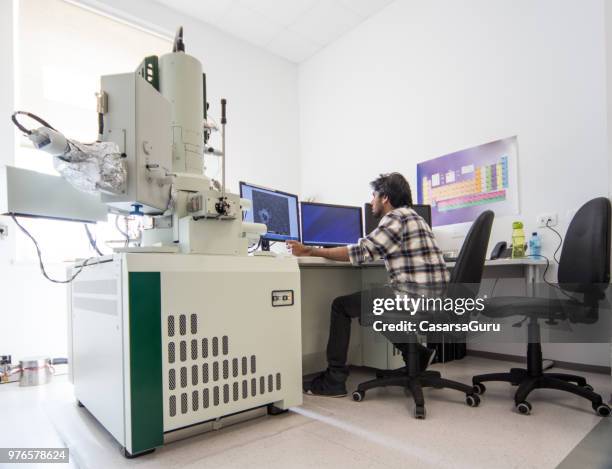 young male scientist using computer next to field emission electron microscope - computer scientist stock pictures, royalty-free photos & images