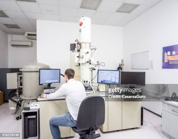 male scientist working on computer while using field emission electron microscope - computer scientist stock pictures, royalty-free photos & images