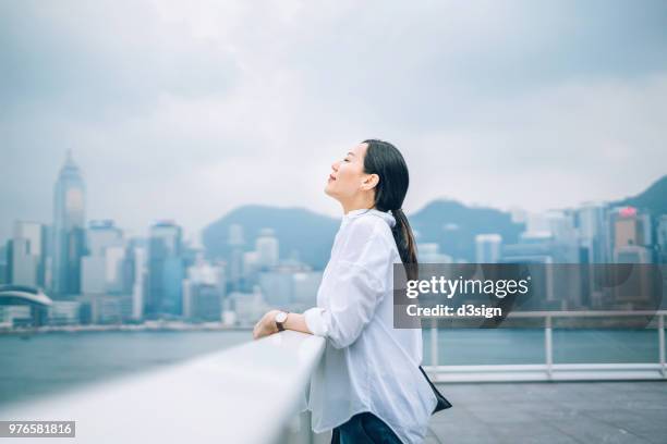 beautiful woman enjoying the fresh air with eyes closed against city background - business air travel photos et images de collection