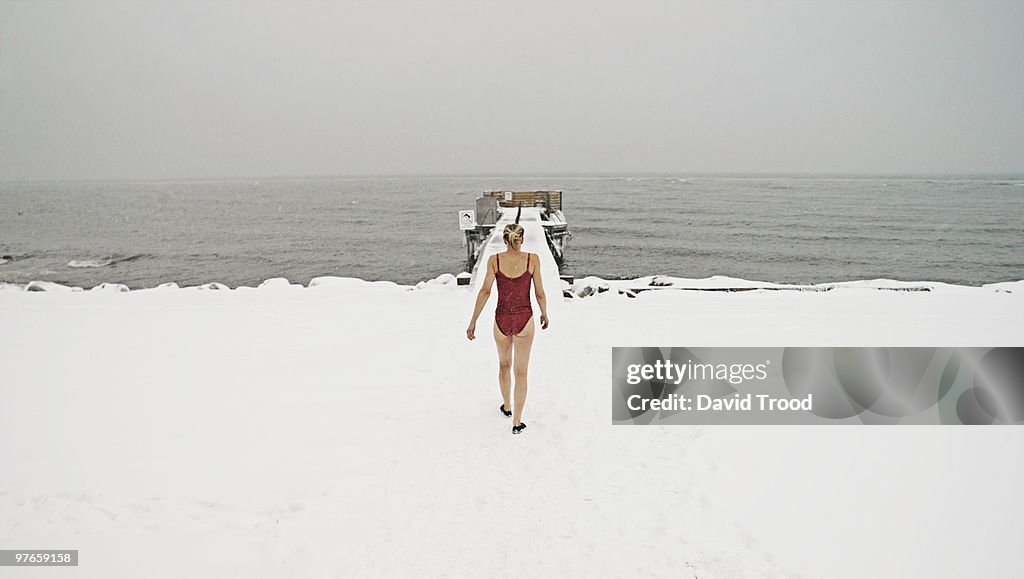 Woman walking towards freezing ocean in bathing su
