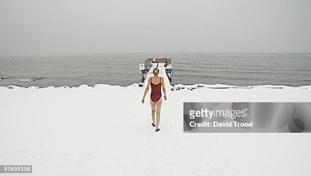 woman walking towards freezing ocean in bathing su - david trood stock pictures, royalty-free photos & images