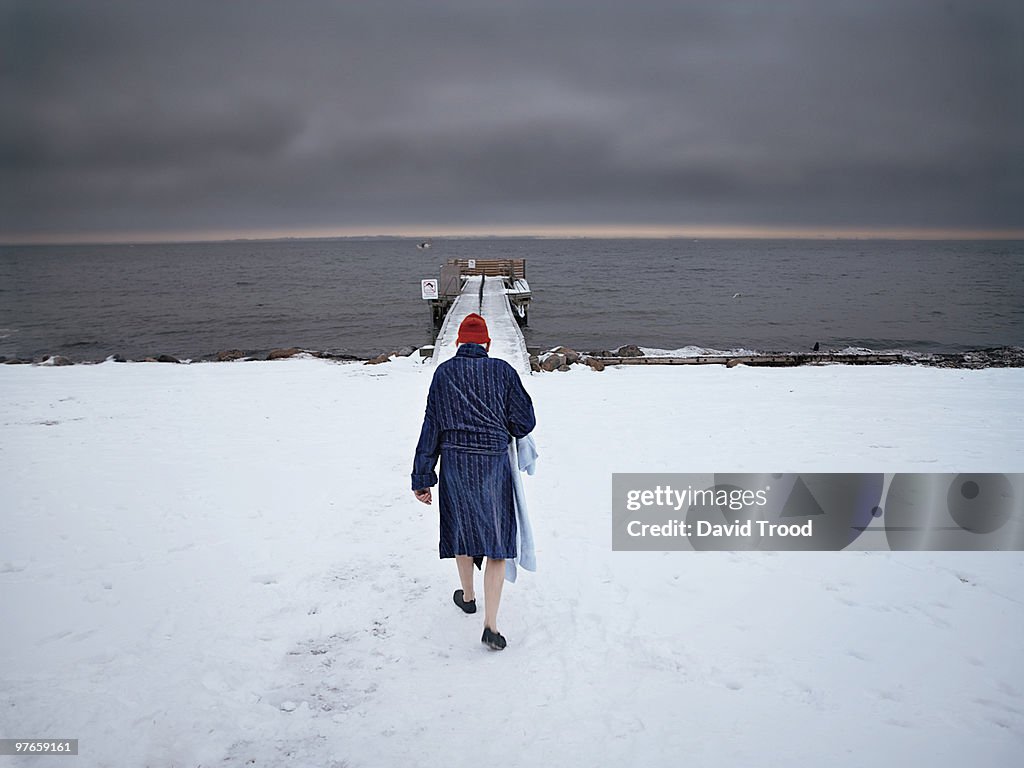 Elderly man walking towards to sea in the snow