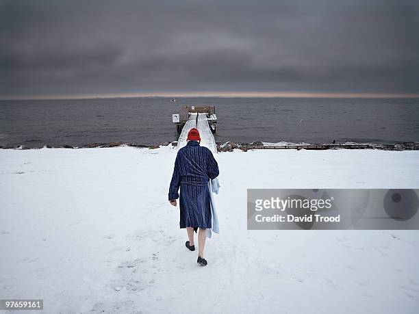 elderly man walking towards to sea in the snow - david trood stock pictures, royalty-free photos & images